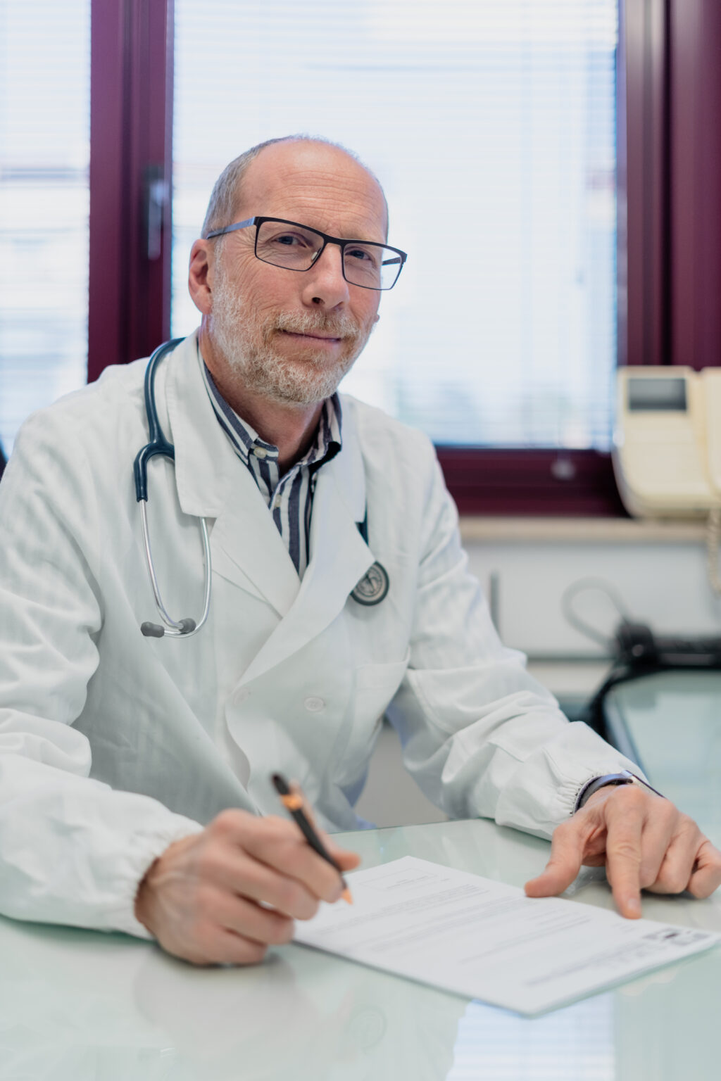 Medico con camice e stetoscopio, seduto alla scrivania dello Studio SMAL